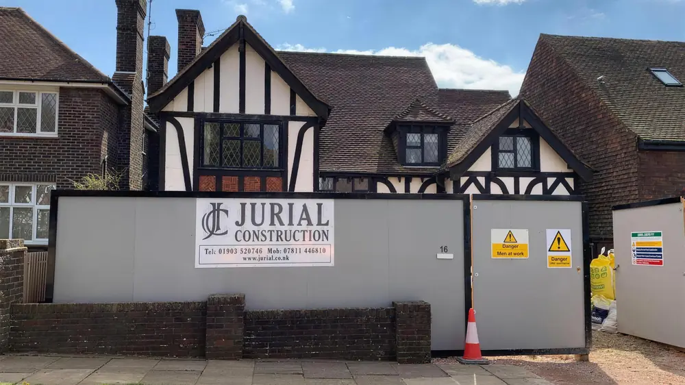 Jurial Construction hoarding with site safety signs and a traffic cone in front of a house in Hove