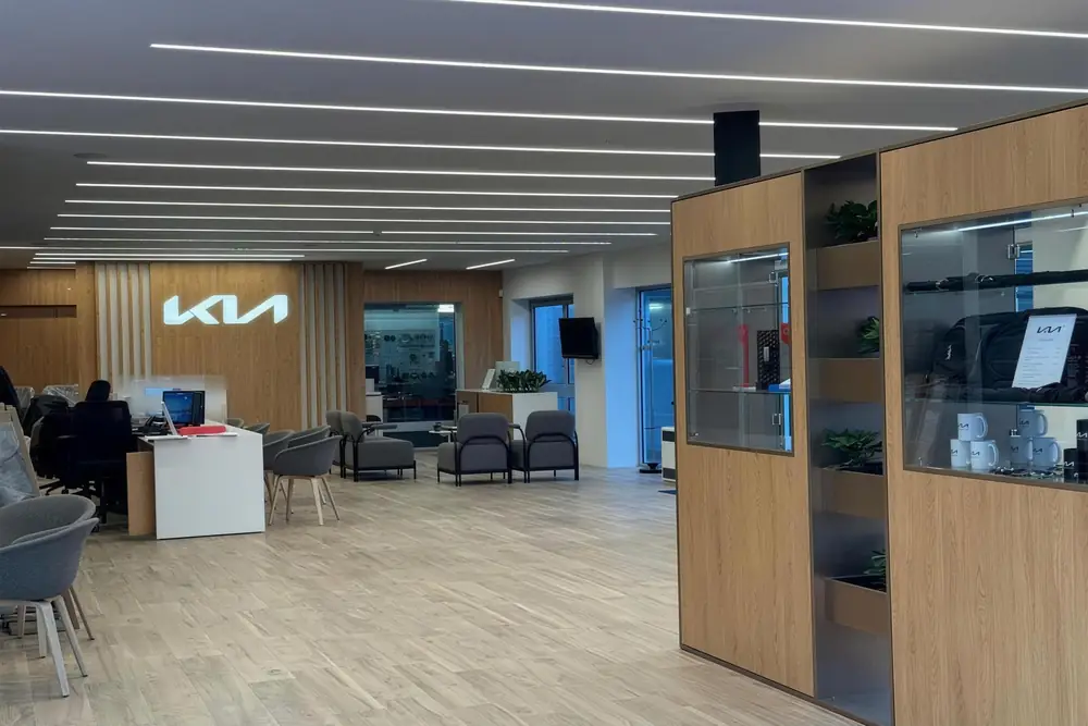 Finished car showroom interior with timber display cabinets, linear ceiling lights and a reception desk beneath an illuminated Kia sign