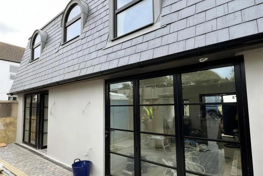 Converted building with arched dormer windows in a slate mansard roof and black-framed glazed doors onto a cobbled courtyard