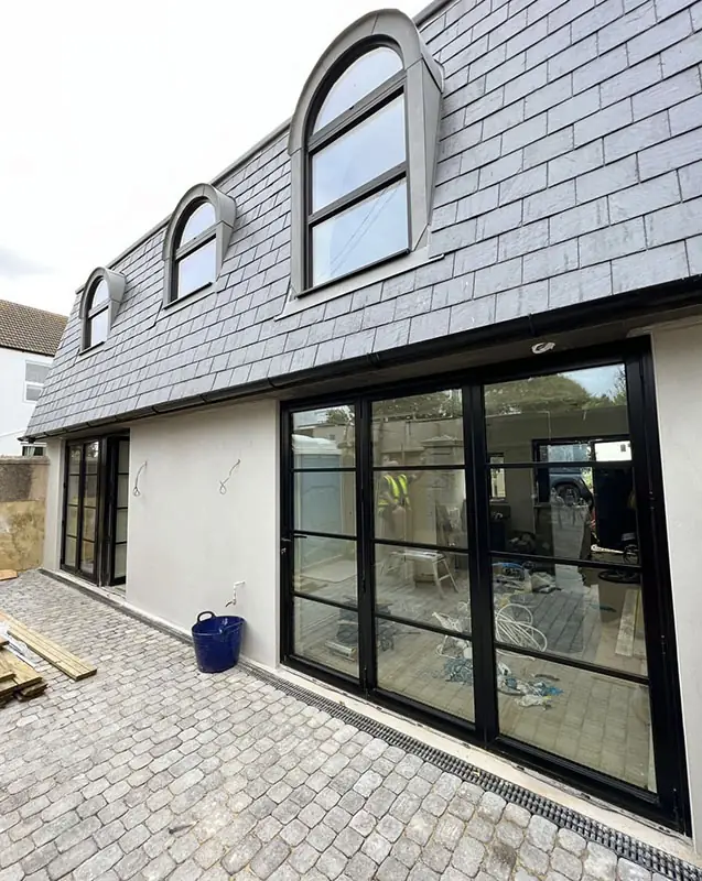 Slate mansard roof with arched dormers and black-framed glazed doors