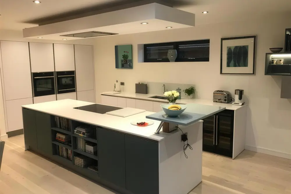 Kitchen with a dark island, white worktops, integrated ovens and a suspended ceiling feature