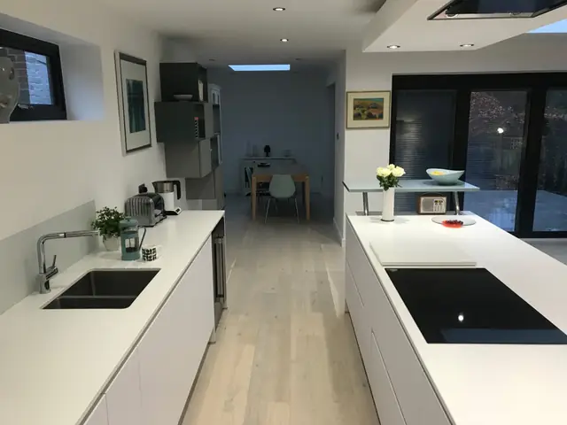 Long kitchen with white worktops leading to the dining area