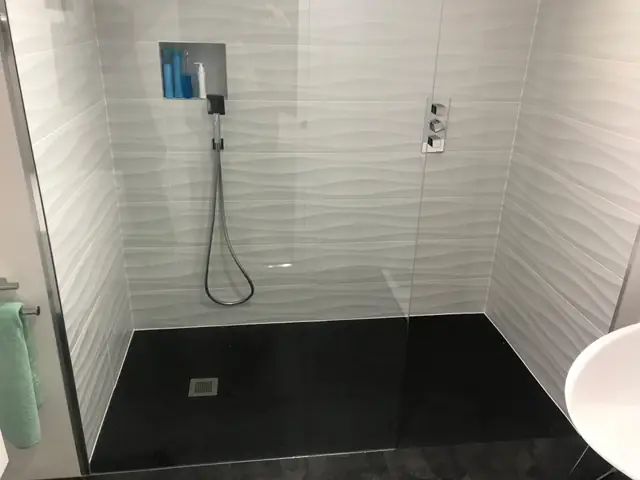 Walk-in shower with textured white wall tiles and a black tray