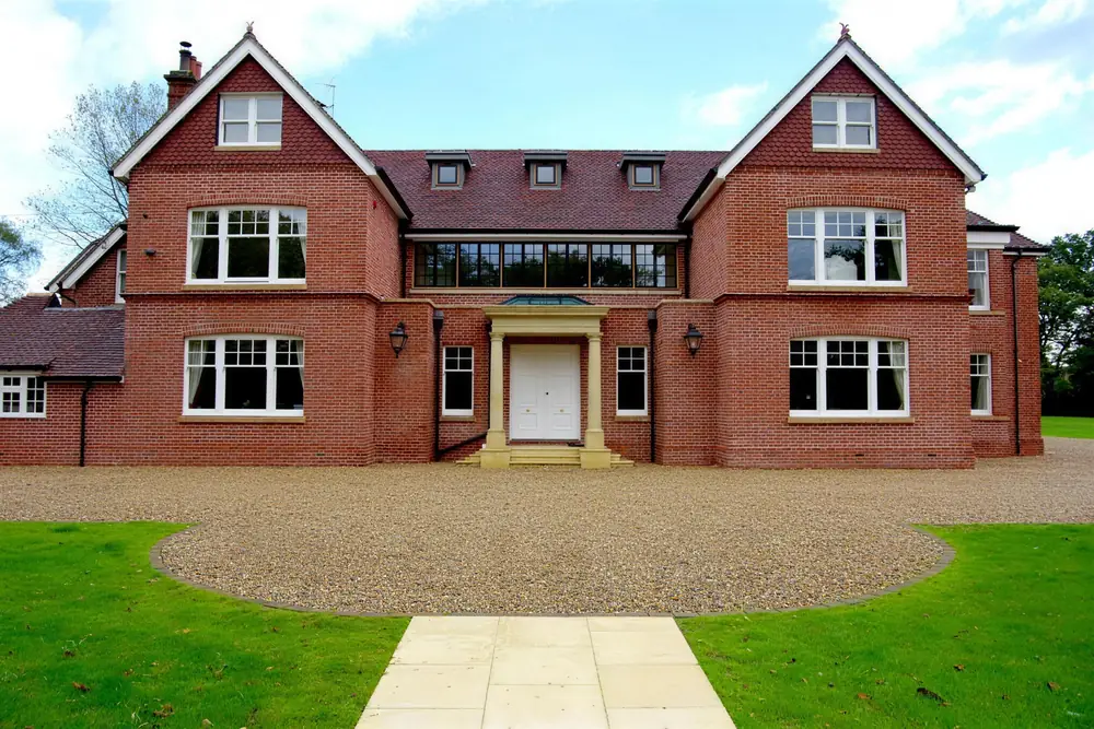 Large red brick Edwardian-style house with gabled wings, a stone door surround and a gravel drive and lawn