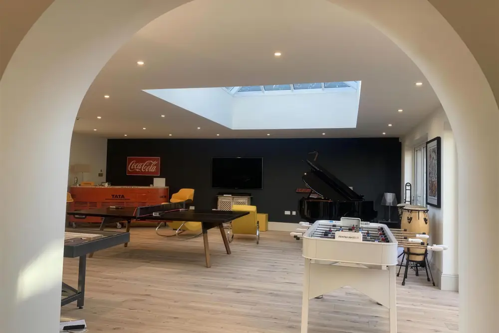 Games room seen through an arched opening, with a roof lantern, oak floor, table tennis table and grand piano